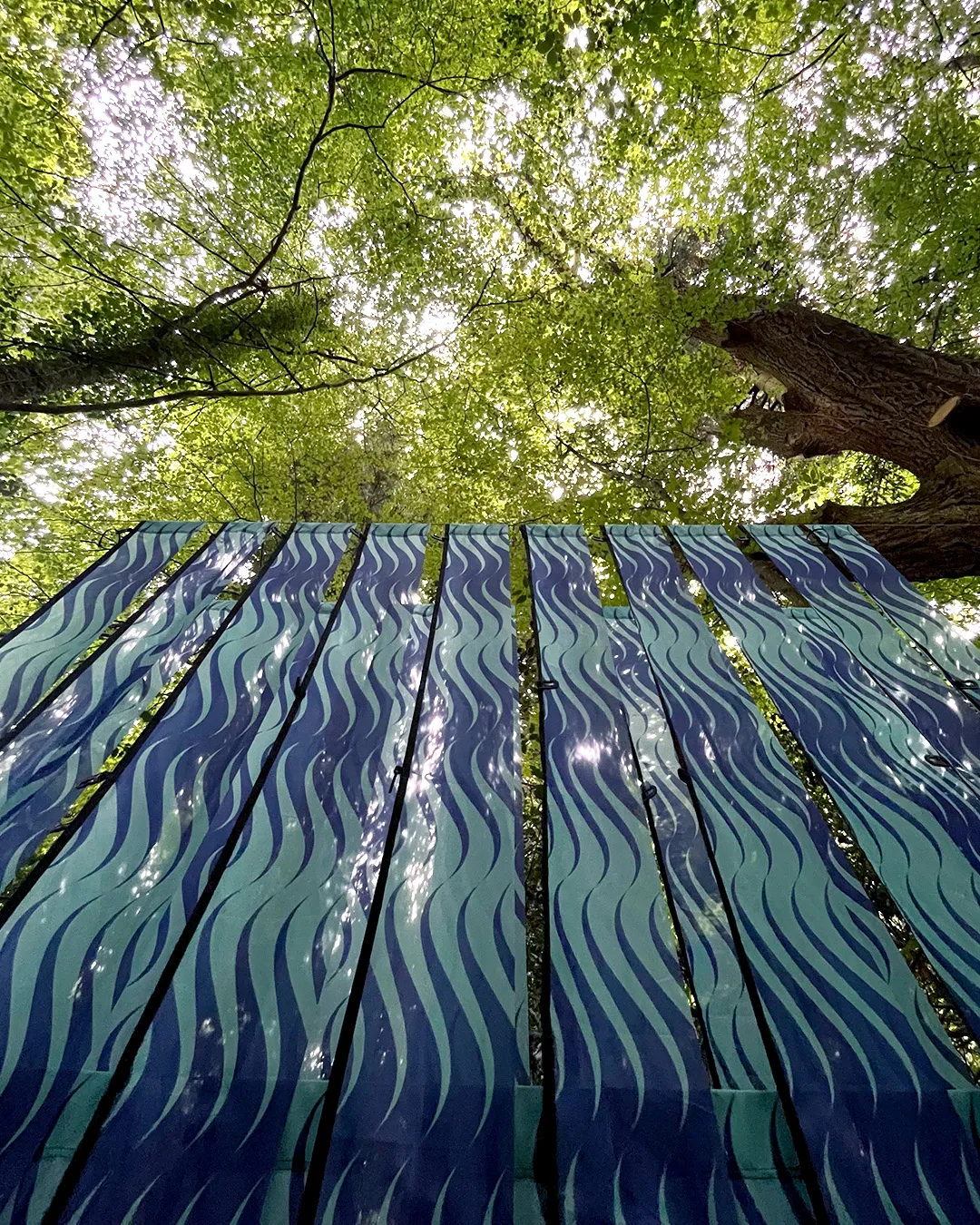 A close up of long strips of a repeat pattern on flag material. The repeat design is seagreen and ultramarine blue waves. 