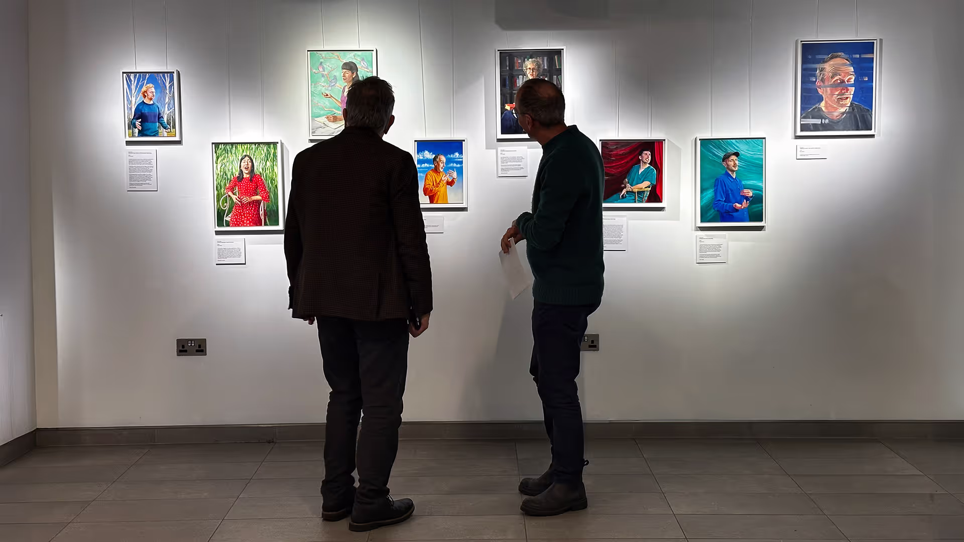 Two men look at hung portraits in an art gallery.
